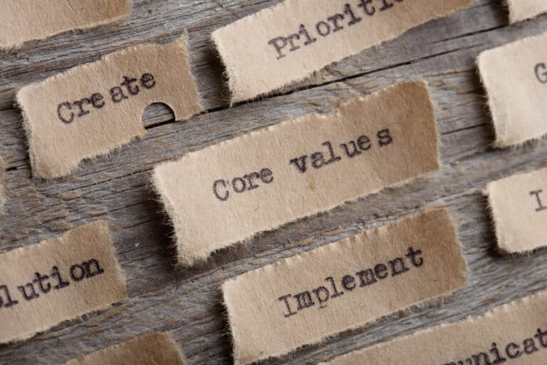 Brown paper strips with words like Core values, Create, Priorit, and Implement are arranged on a wooden surface, representing concepts related to values and strategy—emphasizing the importance of aligning curriculum and school values for a cohesive educational experience.
