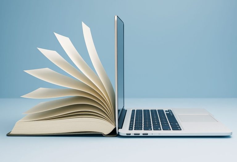 A book with fanned pages stands open beside a slim laptop, their spines and screens touching, symbolizing the connection between traditional books and modern technology in the realm of English Language Arts.